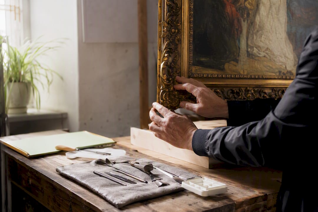 Hands inspecting painting frame in gallery prep room