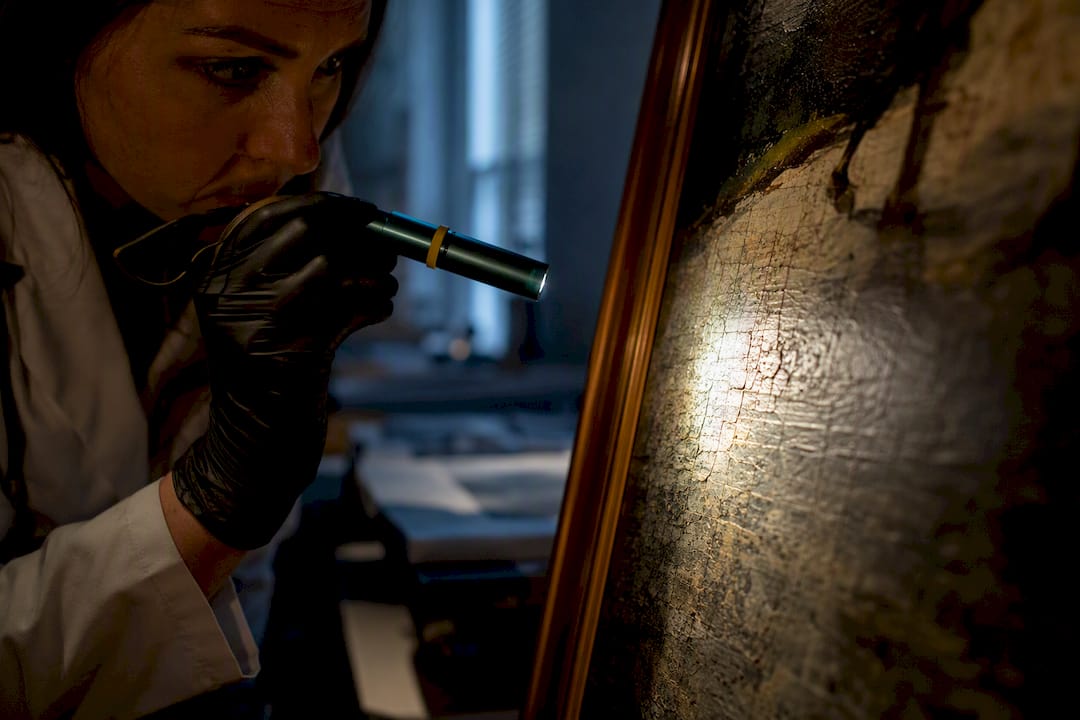 Conservator inspecting painting surface condition